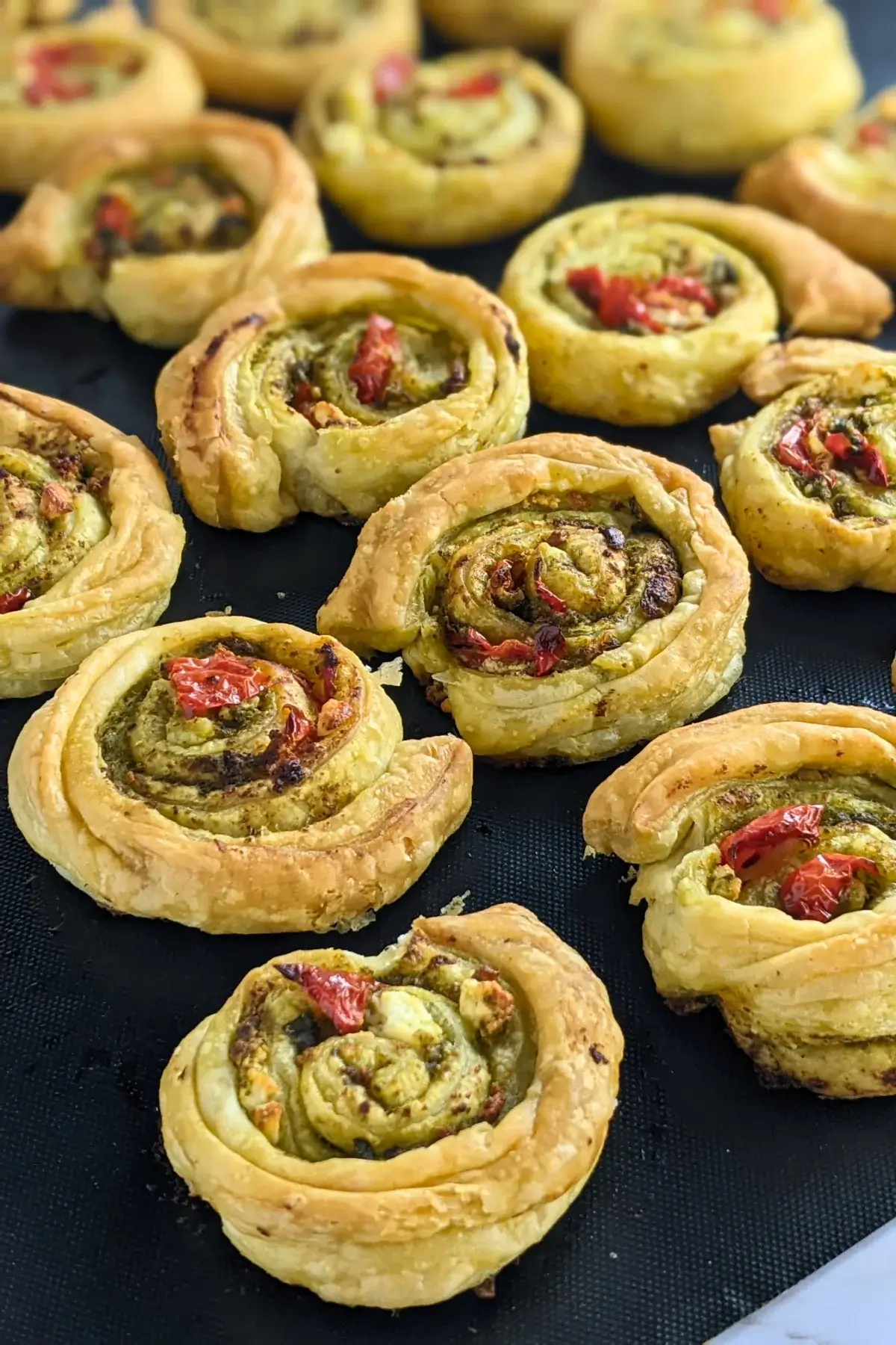 Savory pesto pinwheels made with puff pastry and filled with basil pesto, fresh cherry tomatoes, and crumbled feta.
