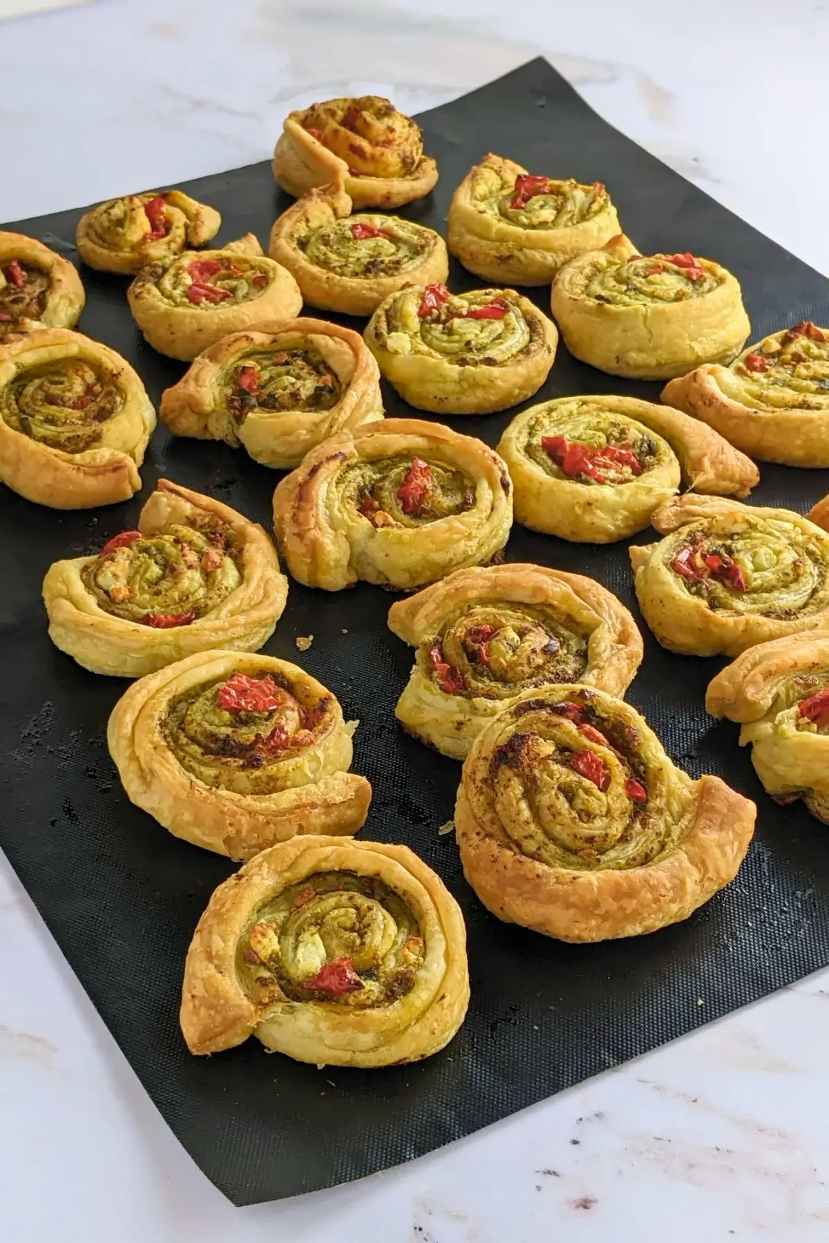 Savory pesto pinwheels made with puff pastry and filled with basil pesto, fresh cherry tomatoes, and crumbled feta.