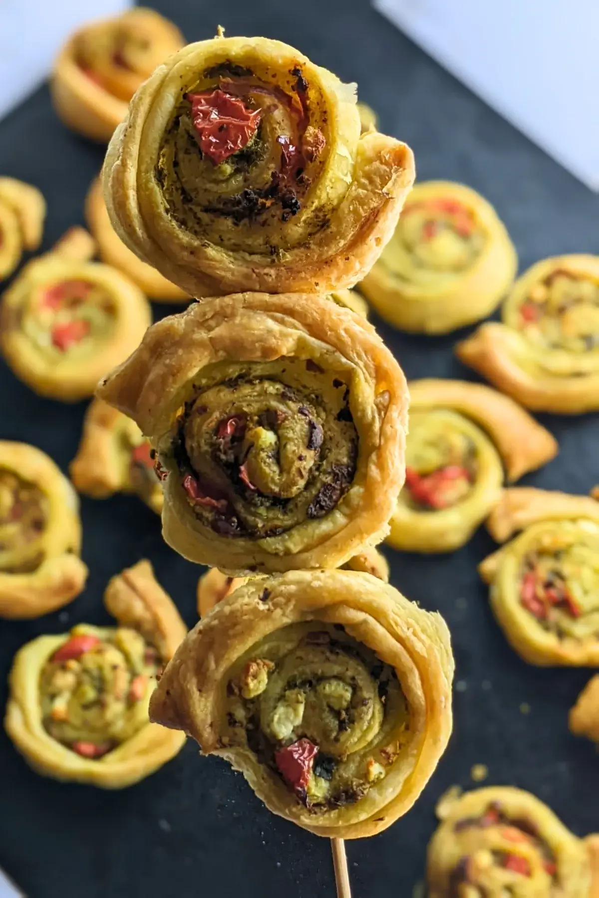 Savory pesto pinwheels made with puff pastry and filled with basil pesto, fresh cherry tomatoes, and crumbled feta.