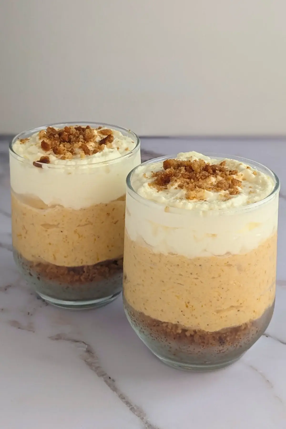Pumpkin yogurt parfait cups layered with pumpkin yogurt, gingersnap biscuits, and topped with whipped cream.