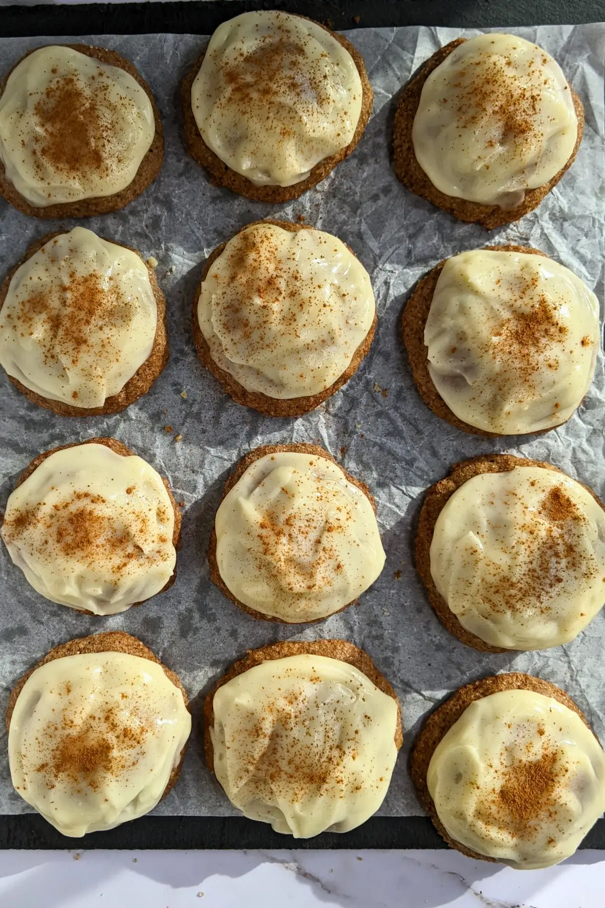 Pumpkin sugar cookies made with healthier wholemeal flour and coconut sugar, frosted with a classic cream cheese icing, and decorated with sprinkles of cinnamon.