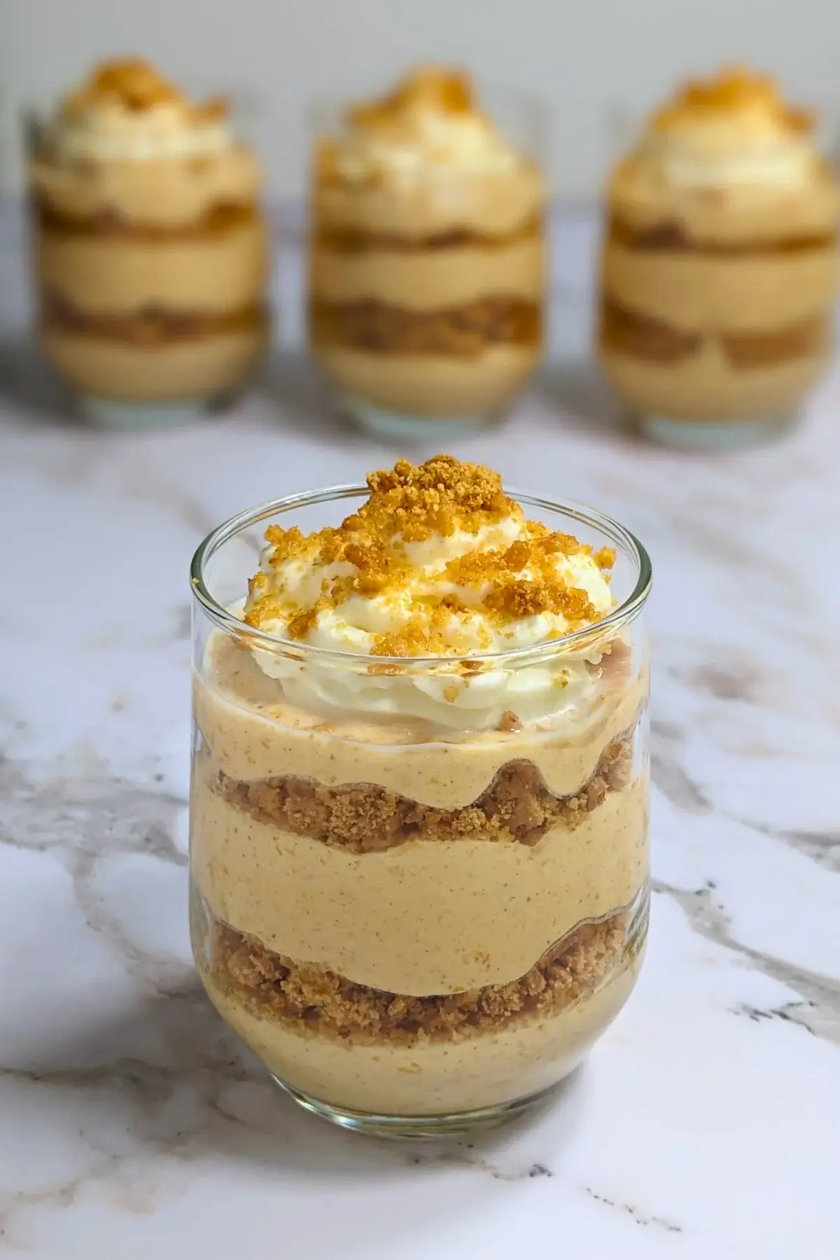 Pumpkin yogurt parfait cups layered with pumpkin yogurt, gingersnap biscuits, and topped with whipped cream.