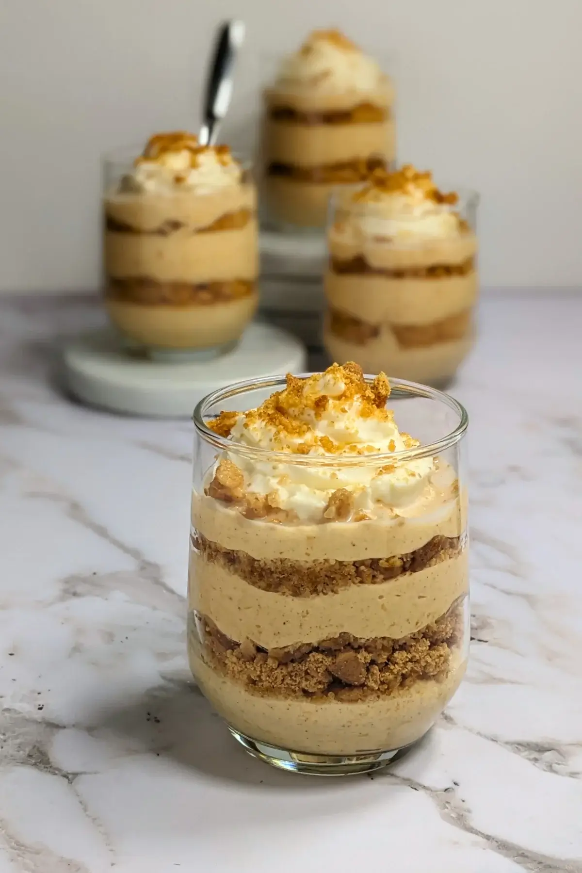 Pumpkin yogurt parfait cups layered with pumpkin yogurt, gingersnap biscuits, and topped with whipped cream.