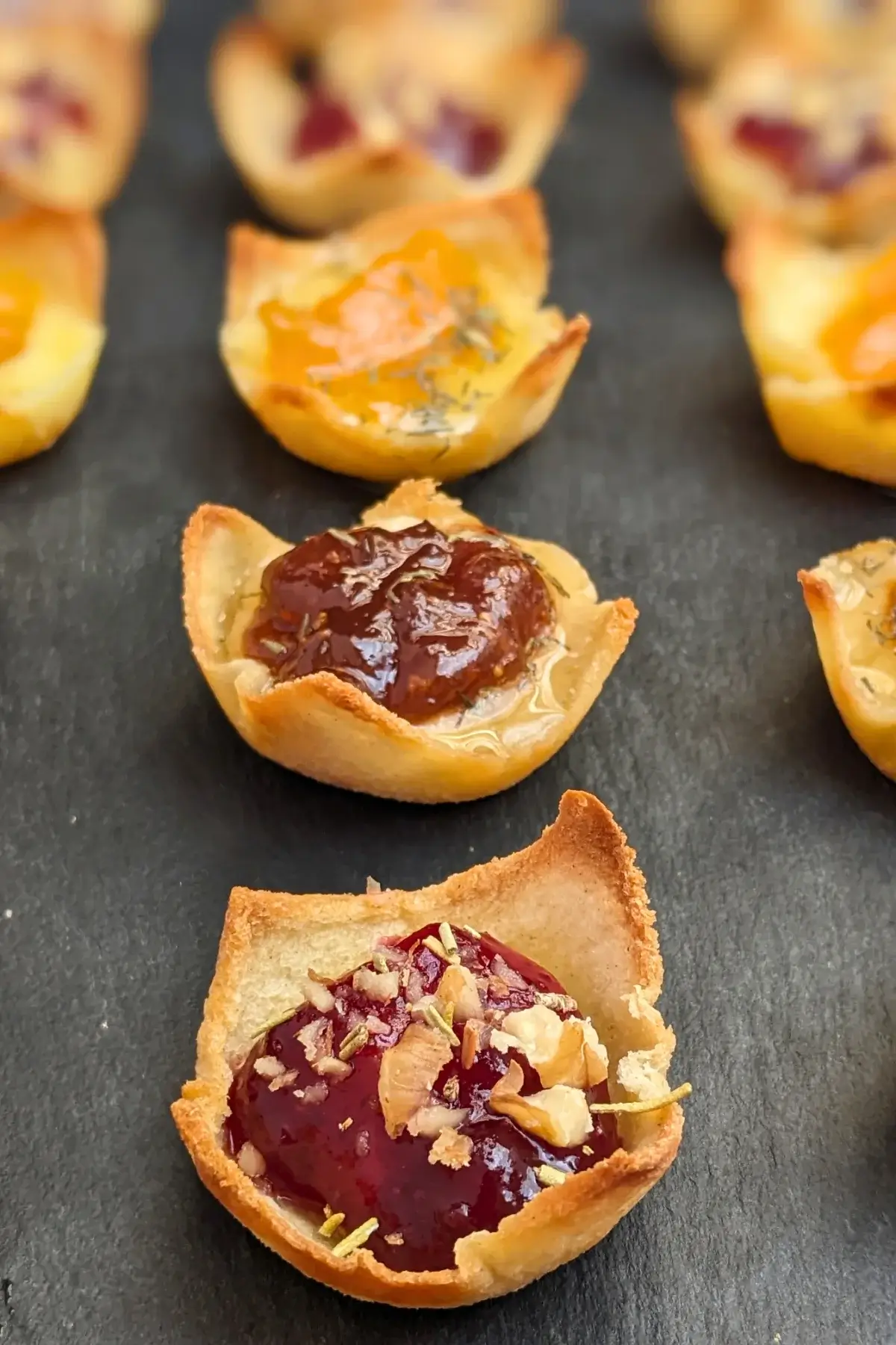 Trio of cheese and jam appetizers in mini toast cups - mini bread toast cups filled with Brie cheese and cranberry jam, Parmesan cheese and fig jam, and cheddar cheese and apricot jam, topped with crushed walnuts and a honey-dried thyme drizzle.