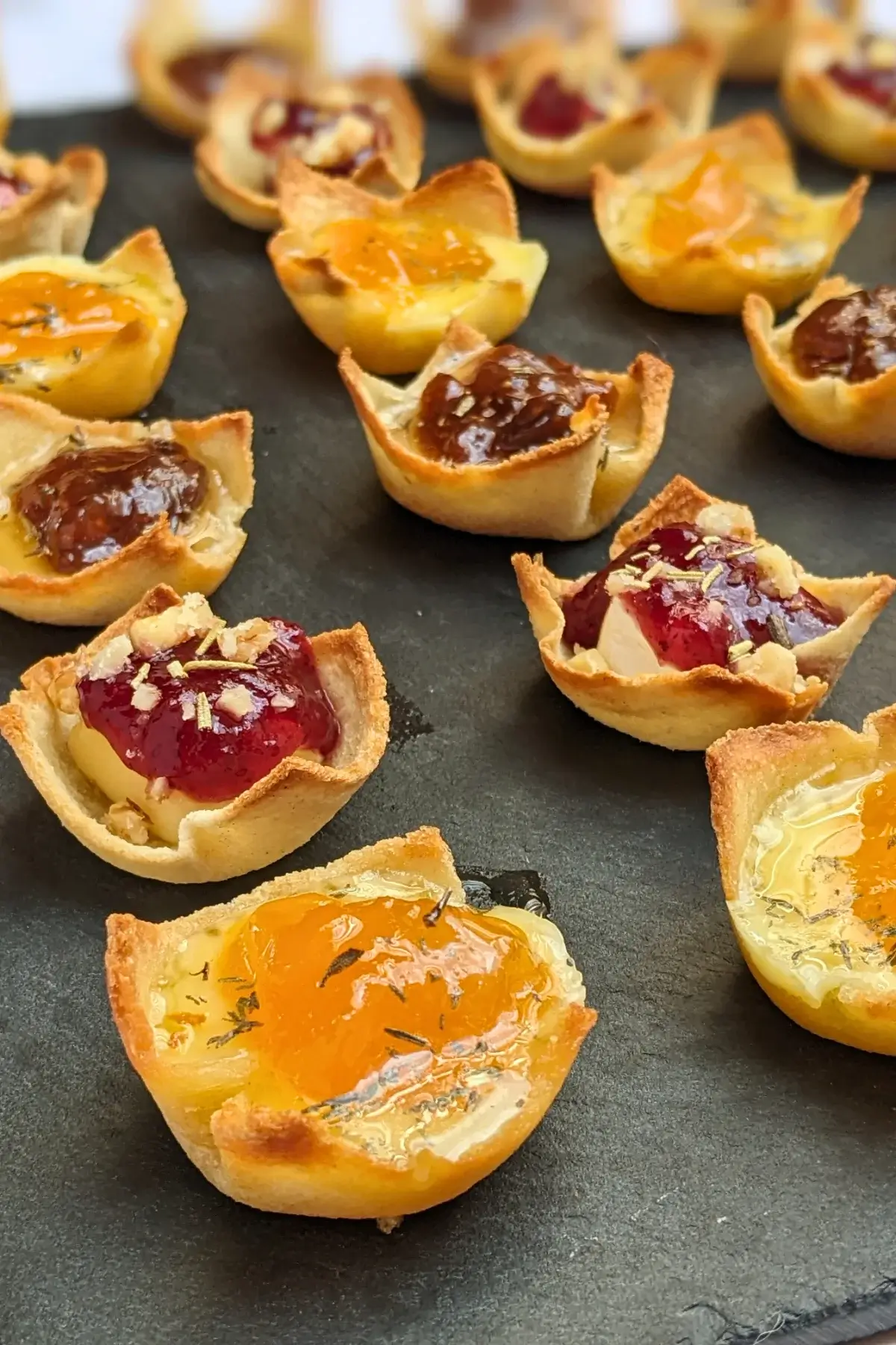 Trio of cheese and jam appetizers in mini toast cups - mini bread toast cups filled with Brie cheese and cranberry jam, Parmesan cheese and fig jam, and cheddar cheese and apricot jam, topped with crushed walnuts and a honey-dried thyme drizzle.